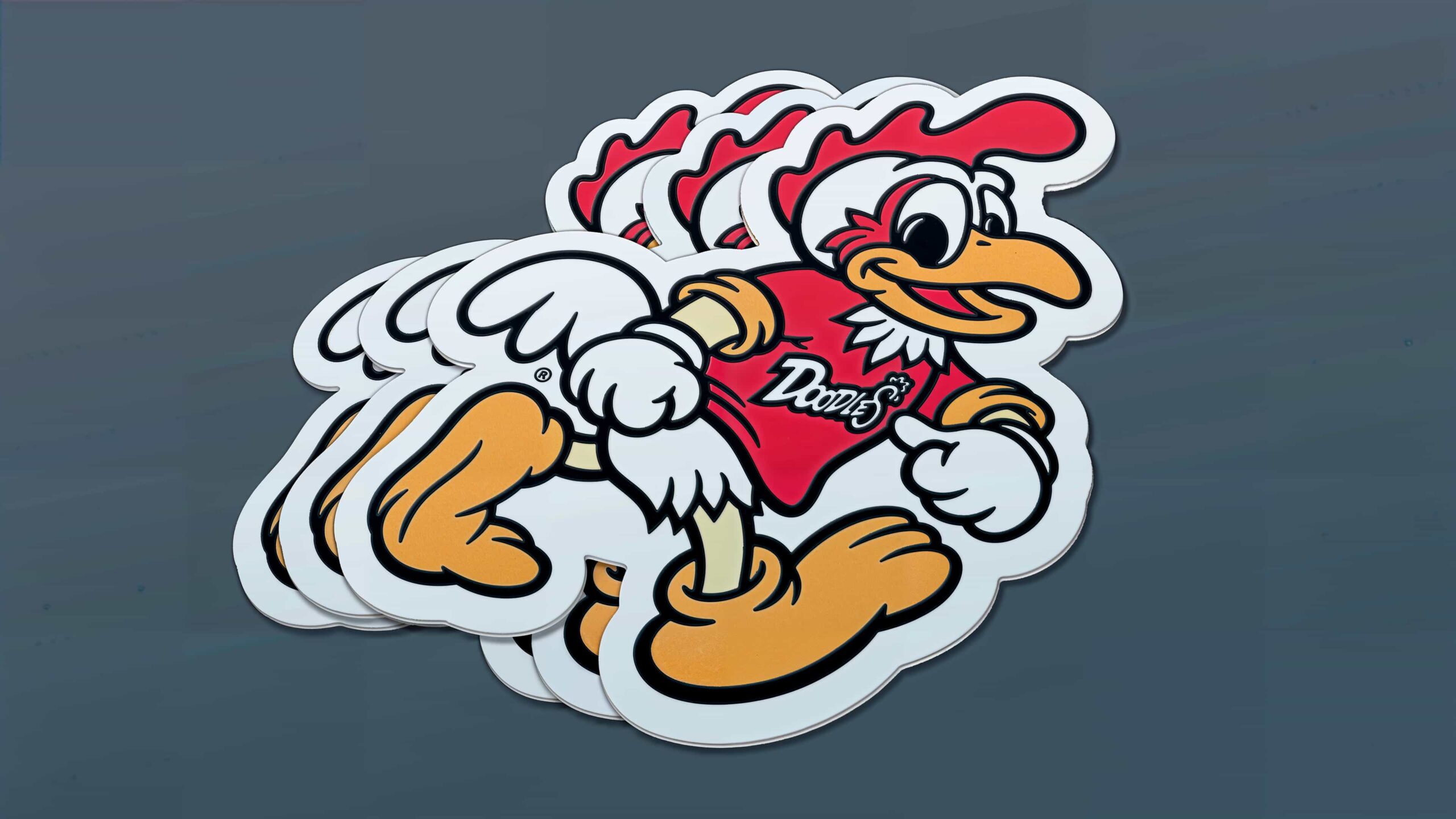 A stack of cartoon chicken character stickers with a red shirt reading "Doodles." The character is depicted in various dynamic poses, with white feathers, orange beak, and feet, and a red comb. The background is a solid dark gray color.